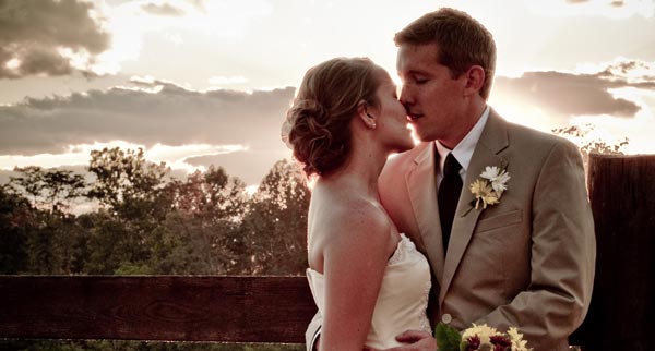 Bride and groom kissing by a fence